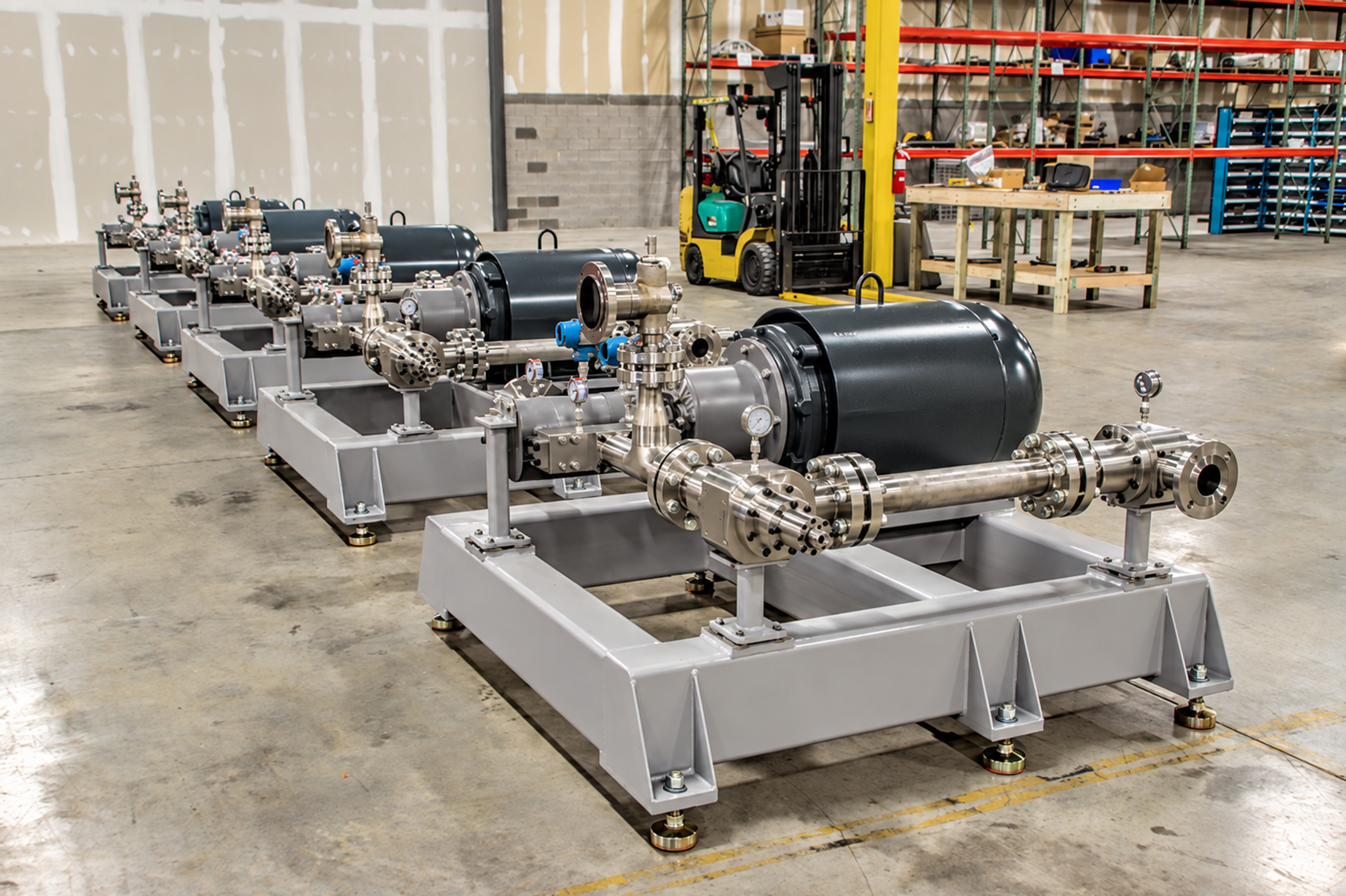 A row of stainless-steel vegetable oil degumming cavitation reactors and motors on rectangular skids in a workshop.